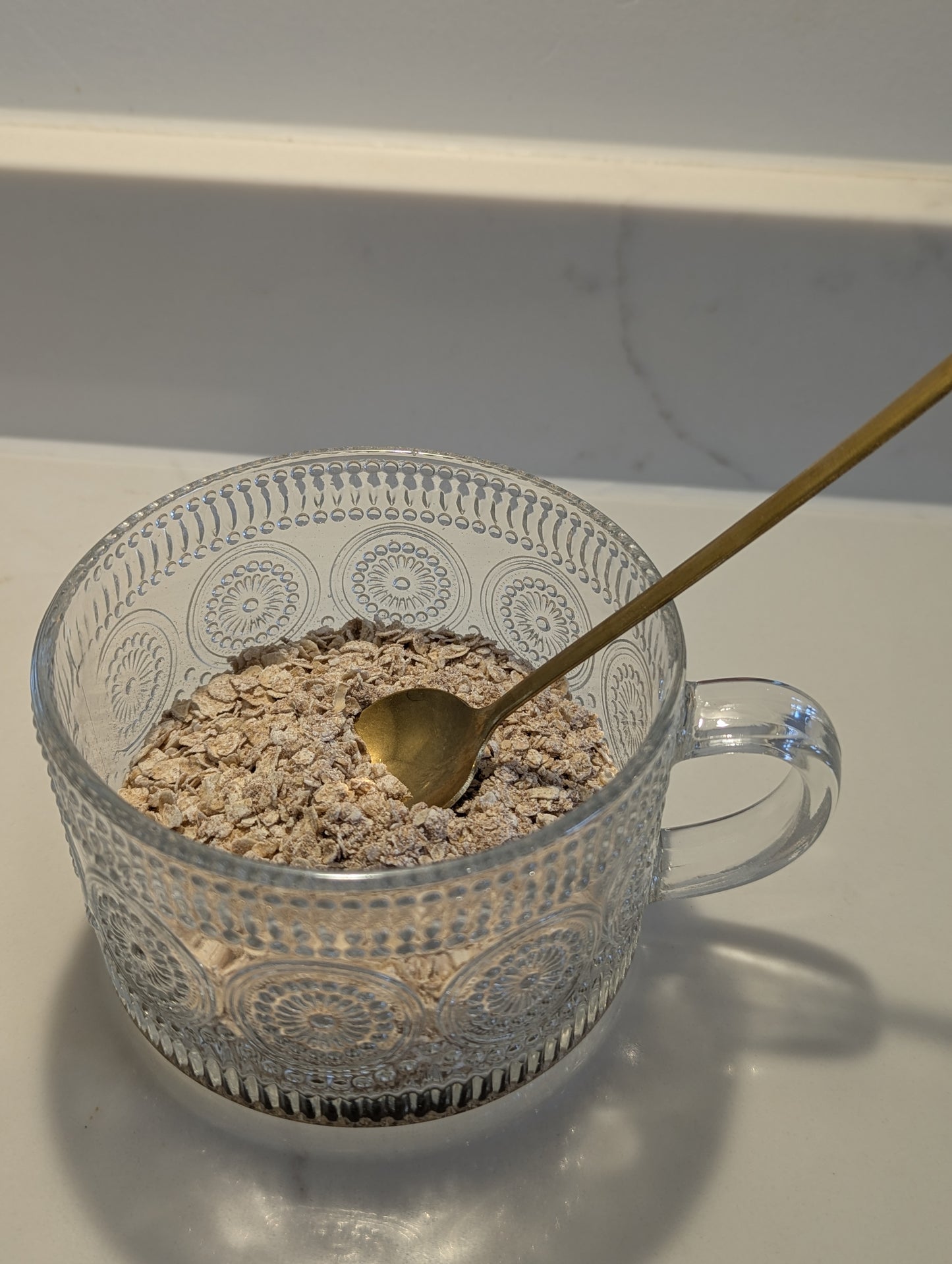 Clear glass bowl with oatmeal and a gold spoon on a white surface