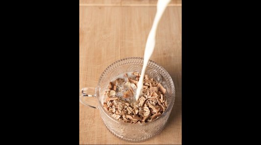 Milk pouring into a bowl of overnight oats on a wooden table