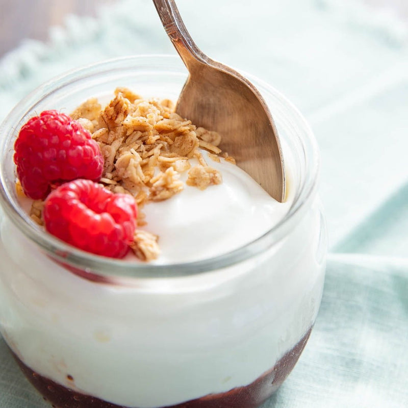 A glass bowl with yoghurt and high-fibre raspberries and oat clusters