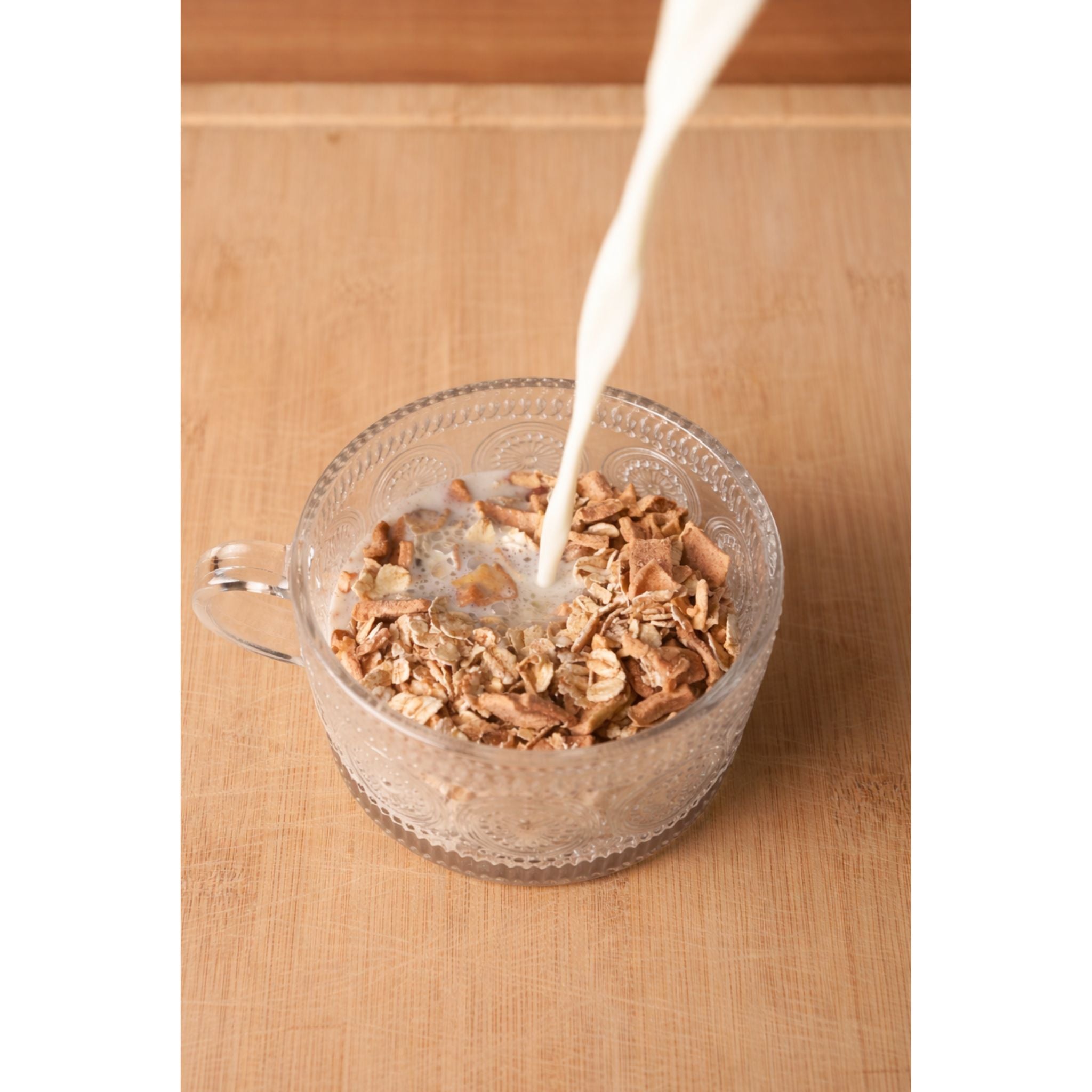 Glass bowl with cereal being poured with milk on a wooden surface
