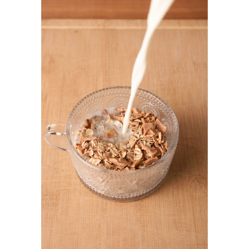 Glass bowl with cereal being poured with milk on a wooden surface