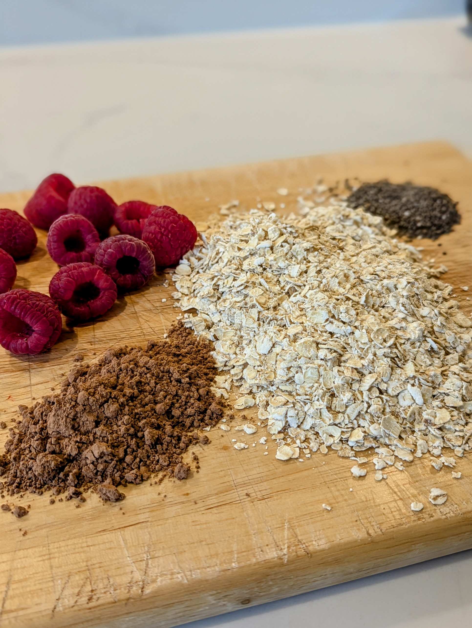 Wooden cutting board with oats, cocoa powder, and raspberries on a light background