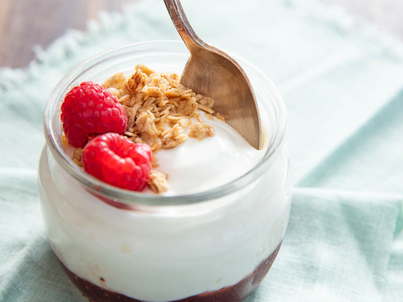 Yoghurt with granola and raspberries in a jar on a light blue fabric background