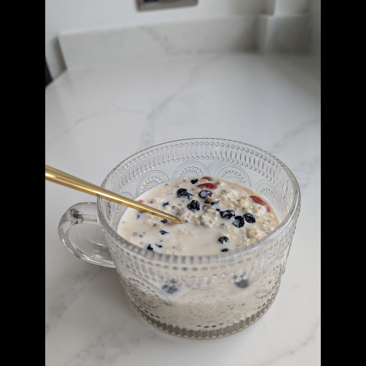 Glass mug of creamy overnight oats with berries and seeds on a white kitchen worktop