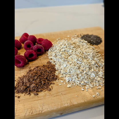 Raspberries, oats, cocoa powder and chia seeds on a wooden board ready to make high fibre porridge