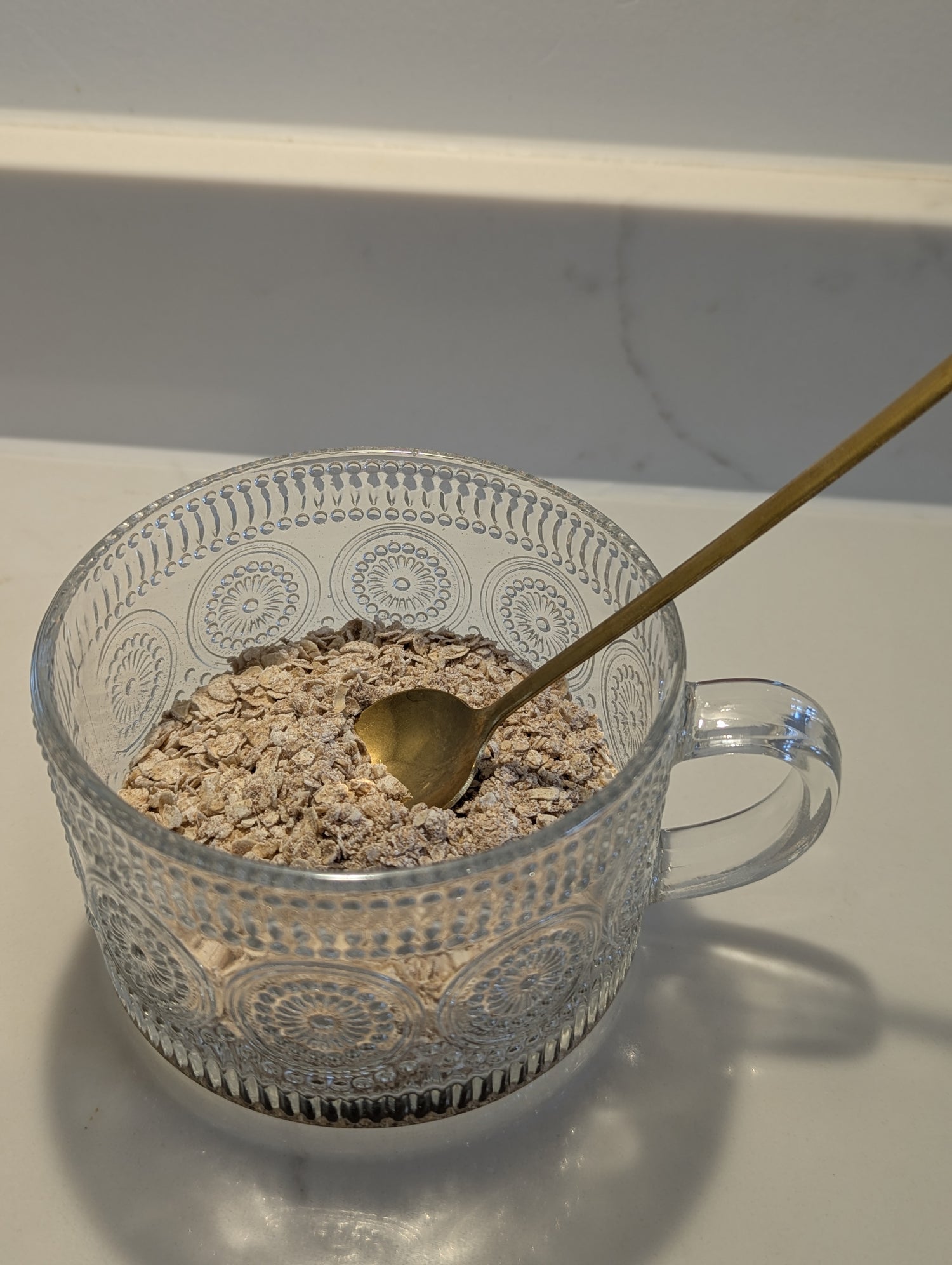 Clear glass bowl with oatmeal and a gold spoon on a white surface