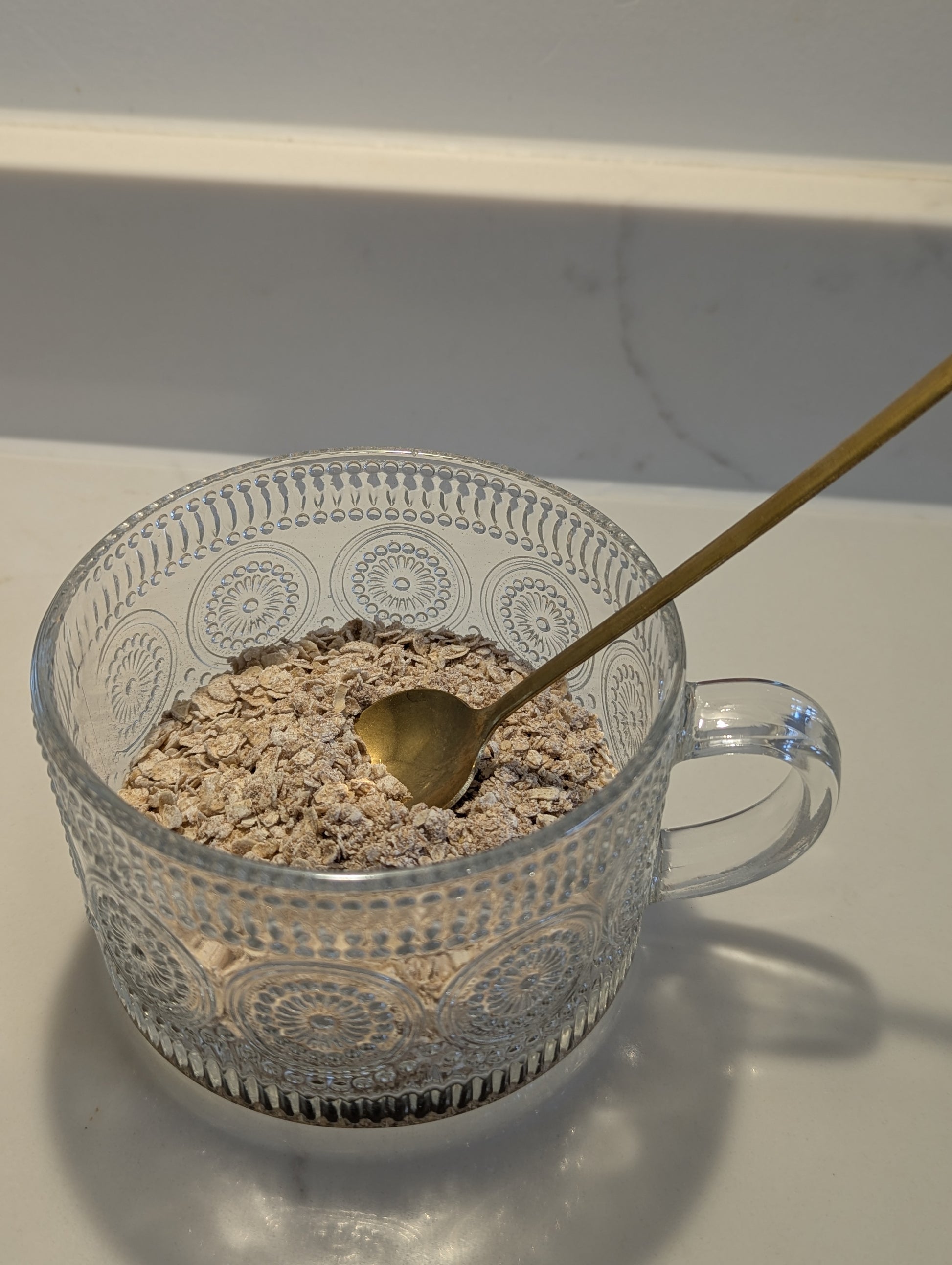 Clear glass bowl with oatmeal and a gold spoon on a white surface