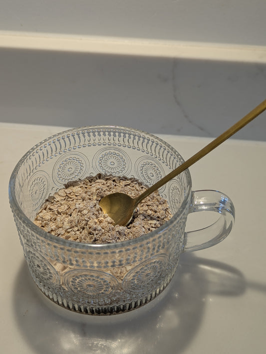 Clear glass bowl with oatmeal and a gold spoon on a white surface